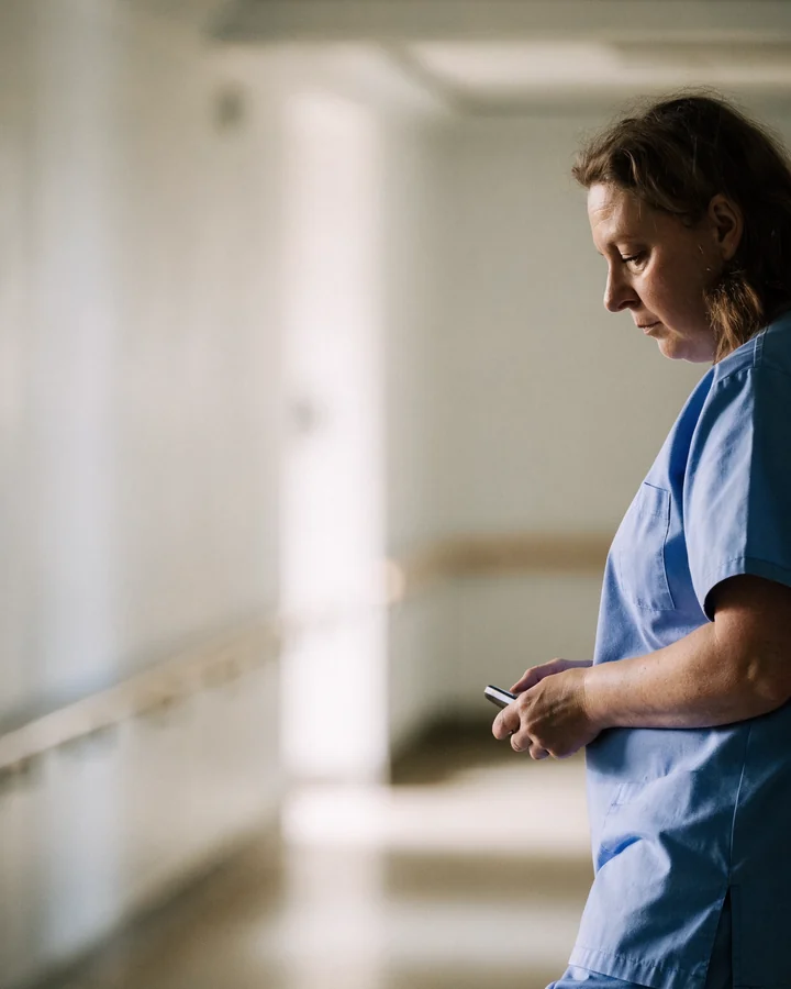 A care worker pausing in a hospital corridor to look at her phone